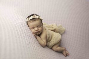 Newborn Baby Girl on a Purple Backdrop hands on face