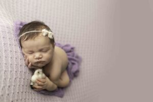 Newborn Baby Girl on a Purple Backdrop hands on face