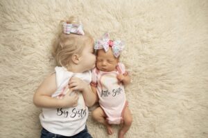 Big sister with newborn baby sister laying down and kissing her