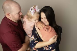 Newborn Baby Girl in pink wrap with Mom and Dad and big sister kissing her