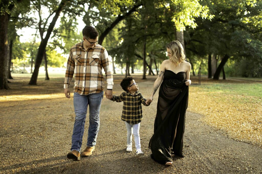 Family portrait session at Trinity Park in Fort Worth, Texas, capturing the family against the backdrop of the park’s scenic views, peaceful trails, and the beautiful Trinity River. The family smiles together as they enjoy the natural beauty, with tall trees and open green spaces providing a serene, picturesque setting. The sunlight filters through the leaves, casting a warm glow on the family, creating a perfect atmosphere for timeless, joyful memories in this tranquil park