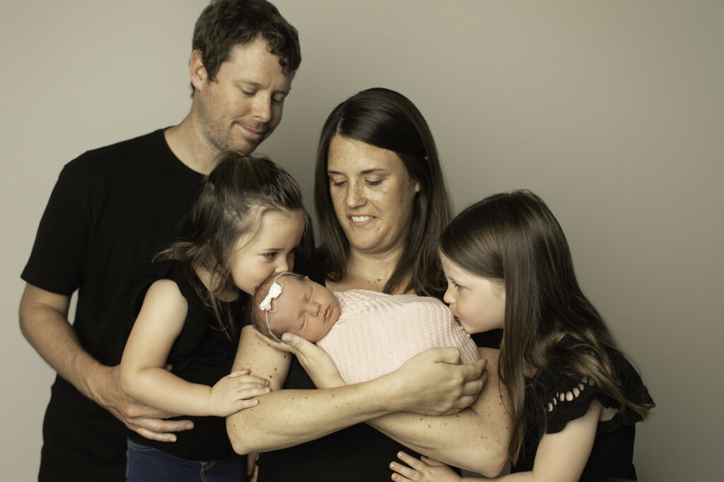 A precious moment captured with a newborn girl surrounded by her loving mom, dad, and two sisters, all smiling in the warmth of their family bond, shot by Chunky Monkey Photography