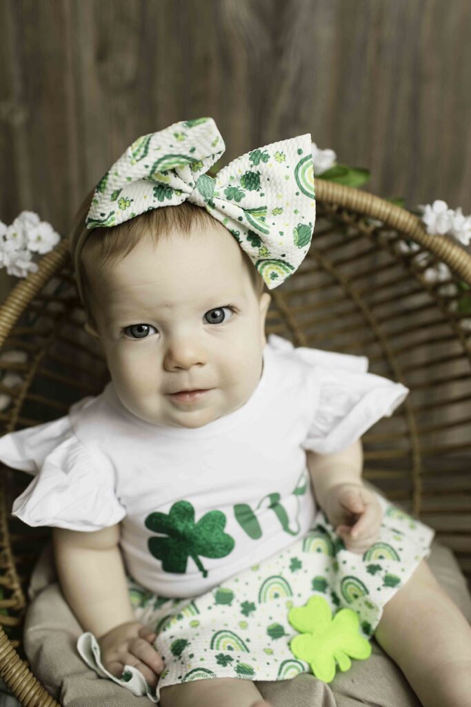 Captured in a whimsical Lucky Clover theme, the one-year-old birthday girl poses sweetly in a wicker chair at Chunky Monkey Photography Studio in Azle, TX