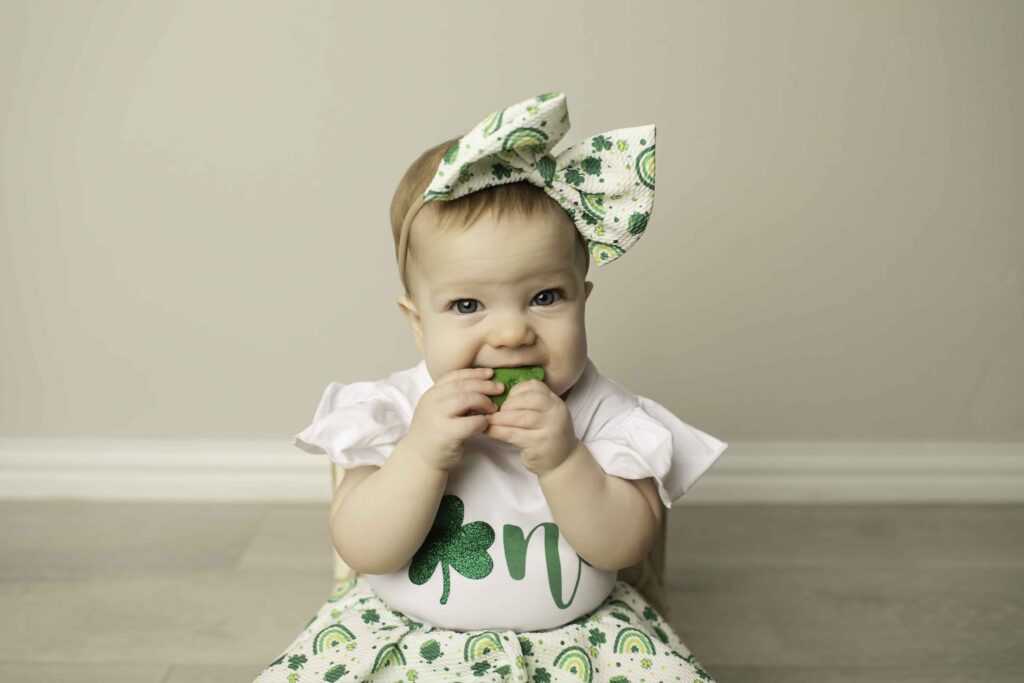 The birthday girl in a green dress sits gracefully in a wicker chair, surrounded by Lucky Clover decor, at Chunky Monkey Photography Studio in Azle, TX.