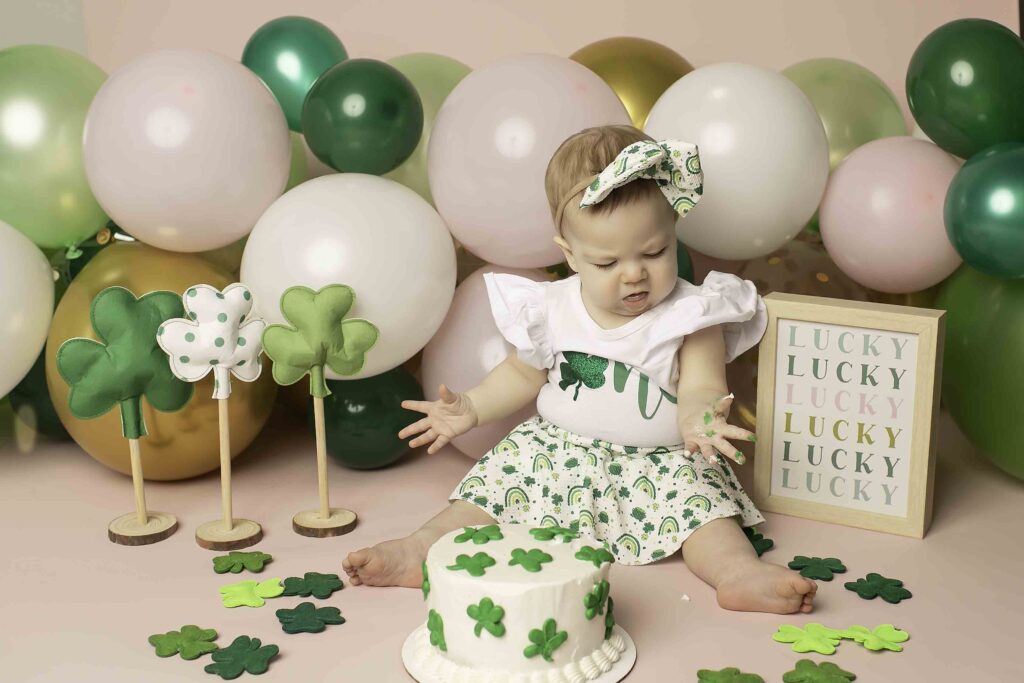 Captured at Chunky Monkey Photography Studio in Azle, TX, the birthday girl in a green dress smashes her cake, creating precious memories in a Lucky Clover-themed setup