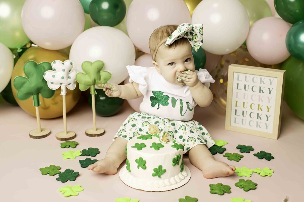 In the Lucky Clover theme, the birthday girl joyfully smashes her cake, surrounded by festive decorations at Chunky Monkey Photography Studio in Azle, TX