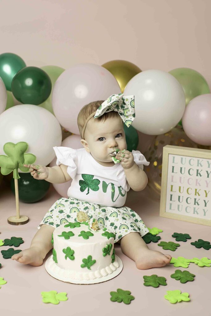 In a whimsical Lucky Clover setting, the one-year-old birthday girl digs into her cake during a cake smash at Chunky Monkey Photography Studio in Azle, TX