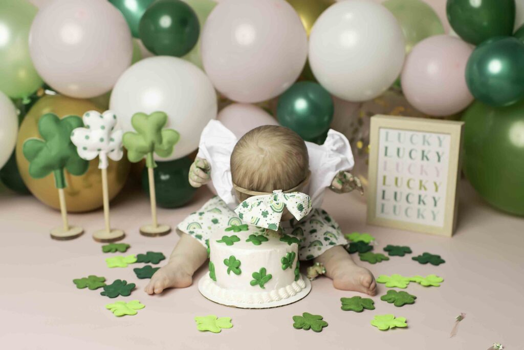 The birthday girl in a green dress enjoys her cake smash in the Lucky Clover theme at Chunky Monkey Photography Studio in Azle, TX, creating sweet memories.