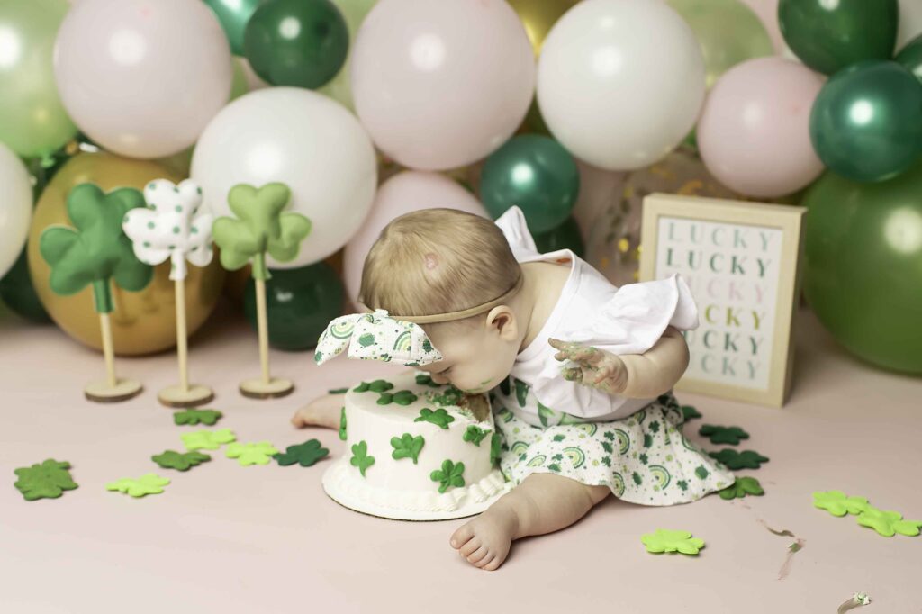 In the Lucky Clover theme, a one-year-old smiles brightly in a green dress, creating magical memories at Chunky Monkey Photography Studio in Azle, TX