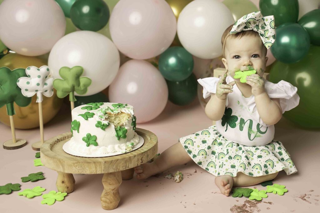 A little one in a festive green outfit sits surrounded by clovers, celebrating their first birthday at Chunky Monkey Photography Studio in Azle, TX