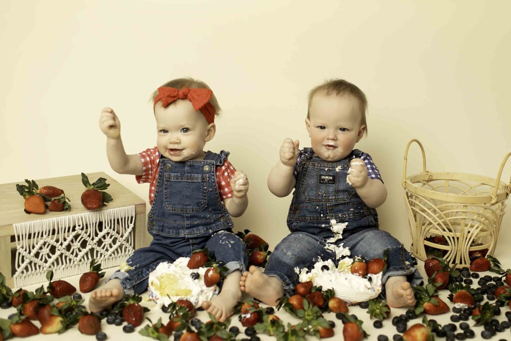 A vibrant twins strawberry smash birthday shoot at Chunky Monkey Photography, featuring adorable siblings covered in pink strawberry frosting and smiles