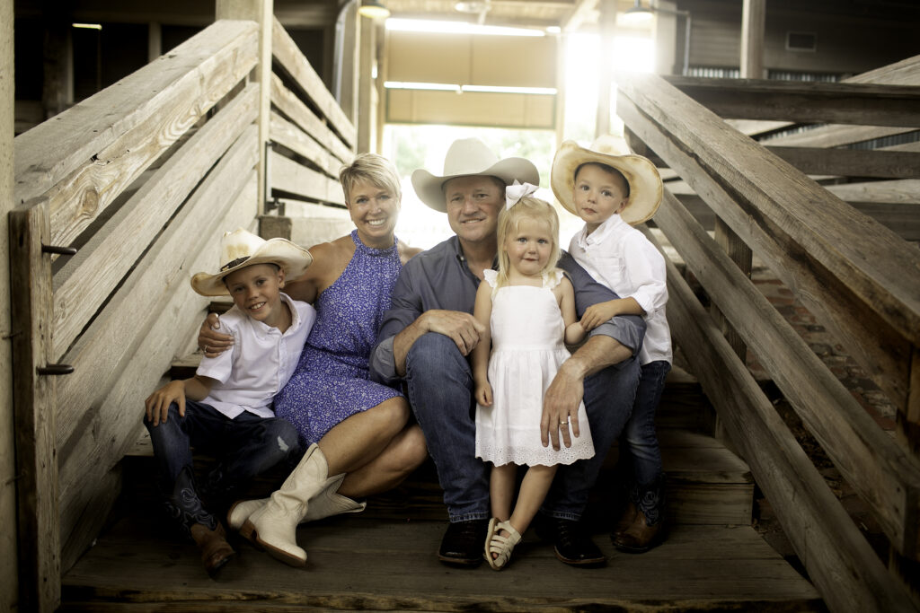 Family portrait session at the Fort Worth Stockyards, capturing the family against the backdrop of historic brick buildings, rustic wooden fences, and classic western charm. The vibrant atmosphere of the Stockyards, with its unique blend of history and cowboy culture, creates a fun and memorable setting. The family smiles together, embracing the rustic elegance and timeless spirit of the area, making for a truly unforgettable moment in this iconic Fort Worth landmark