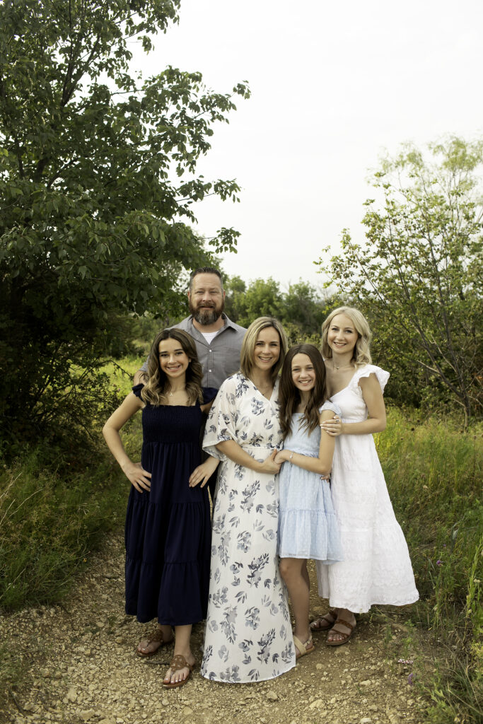 A family of five posing at Tandy Hills, Fort Worth, as three sisters share a touching moment before the oldest leaves for college, surrounded by the beauty of nature