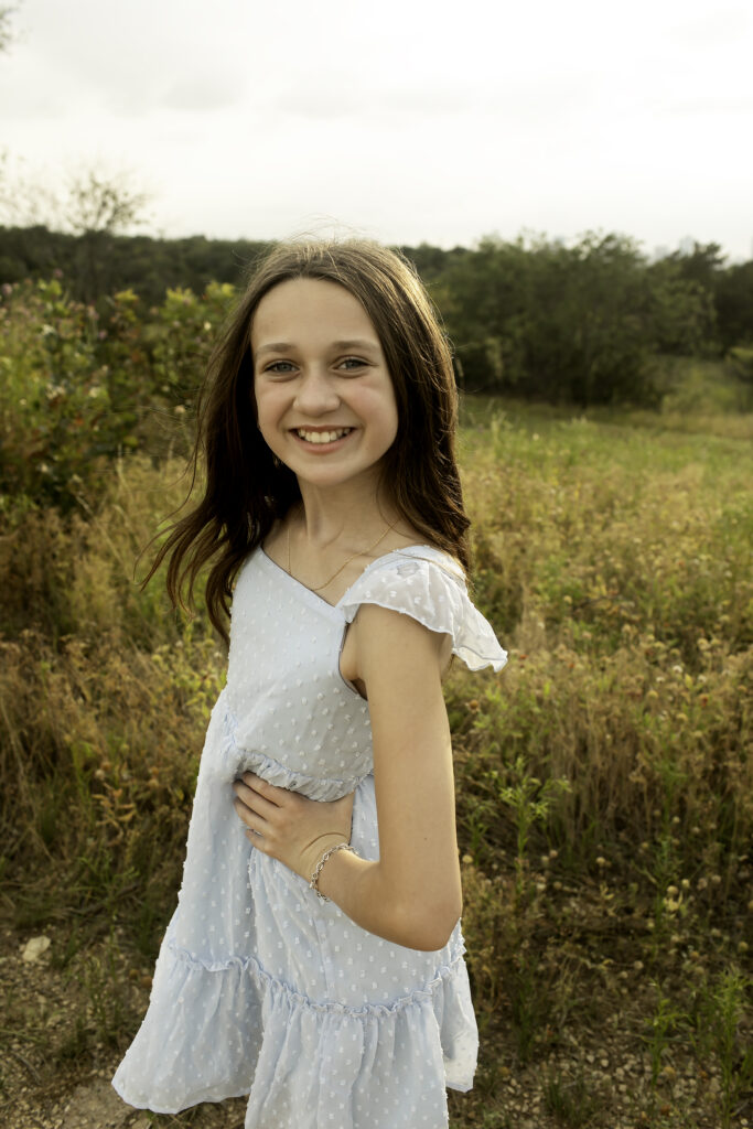 The youngest sister playfully standing on the hills of Fort Worth, full of energy and excitement, cherishing every moment spent with her older sisters before their paths shift.