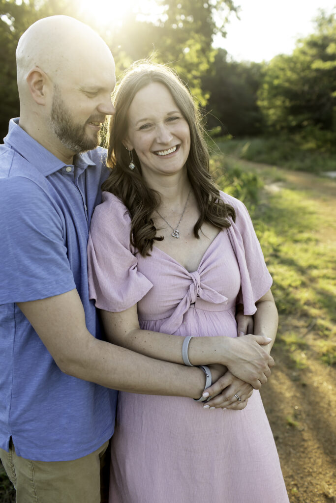 Pregnant couple smiling and enjoying a serene moment together in a beautiful park, capturing their love and excitement