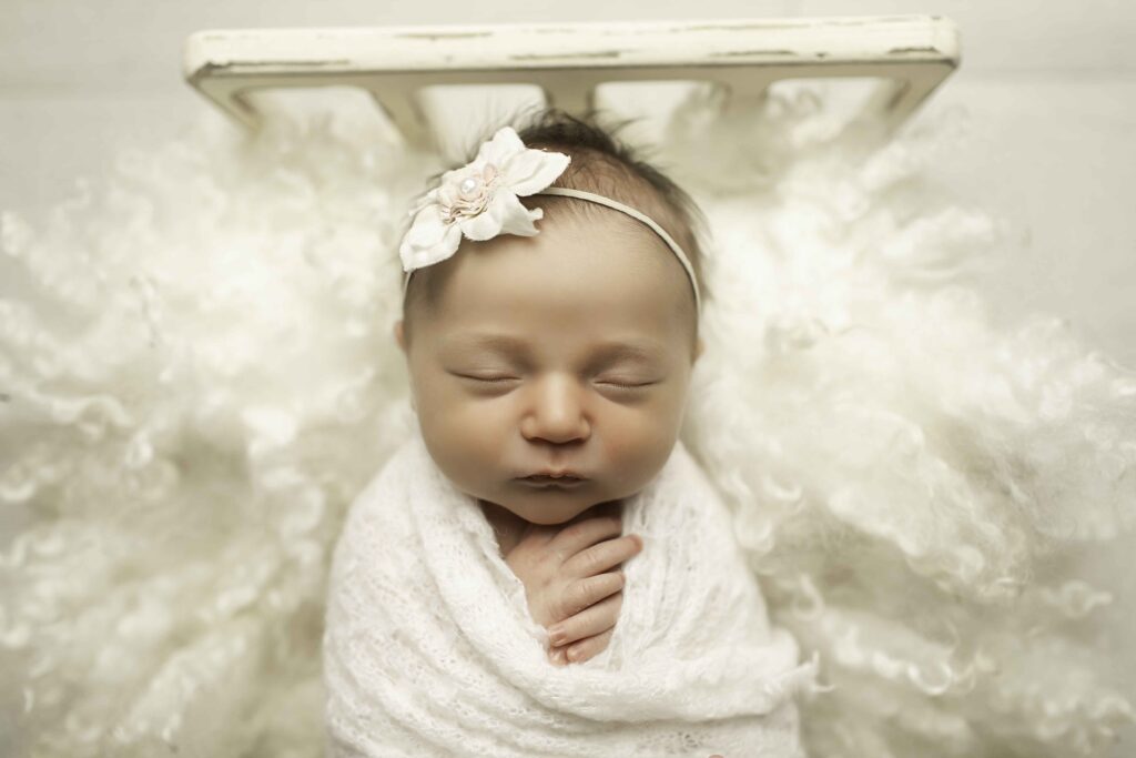 A newborn girl peacefully resting in a soft bed, wrapped in cozy blankets, captured in a serene moment by Chunky Monkey Photography