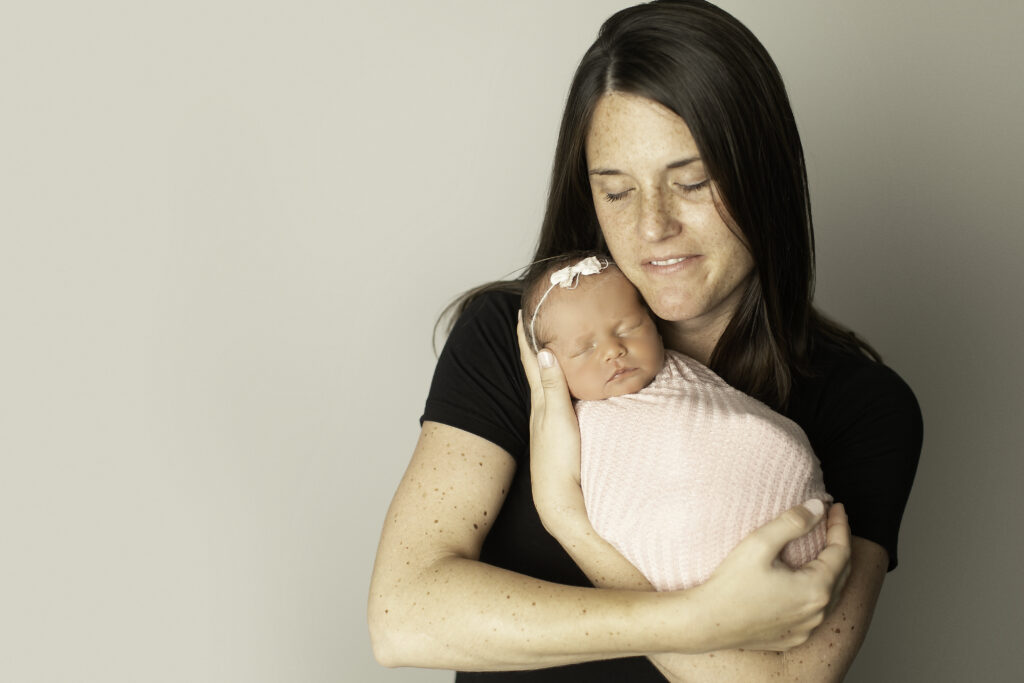 A mom’s love shines as she lovingly holds her newborn girl, captured in a heartwarming moment by Chunky Monkey Photography