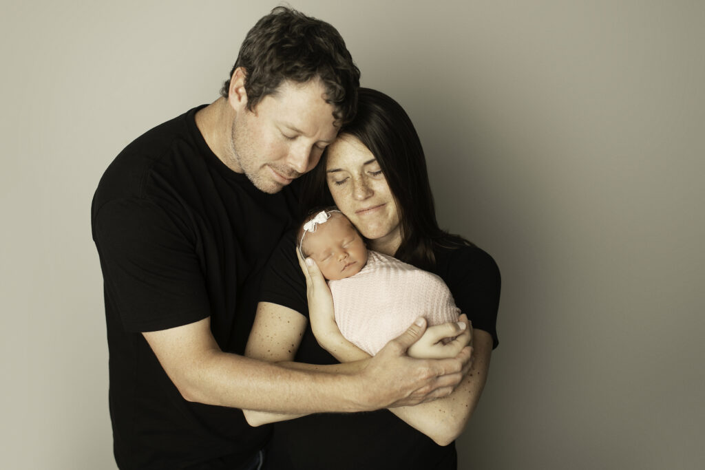 A proud mom and dad lovingly surround their newborn girl, celebrating their new addition in this peaceful family moment captured by Chunky Monkey Photography