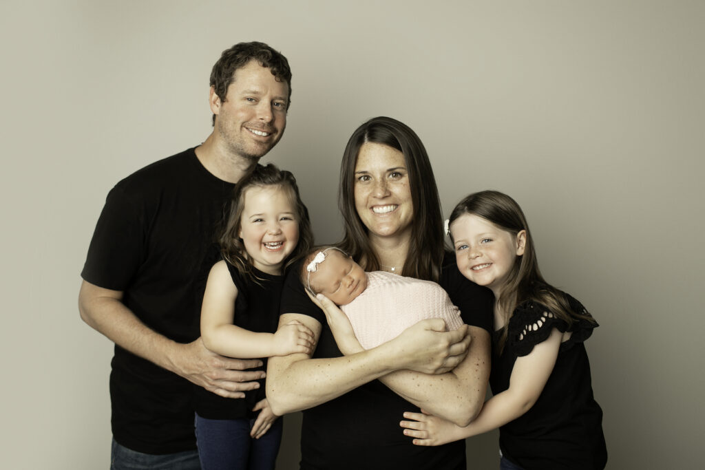 The whole family gathered around their newborn girl, with mom, dad, and two sisters sharing a tender moment of love and joy, beautifully captured by Chunky Monkey Photography.