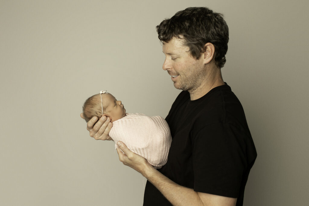 Dad lovingly holds his newborn girl, captured in a peaceful moment of connection and love, beautifully shot by Chunky Monkey Photography