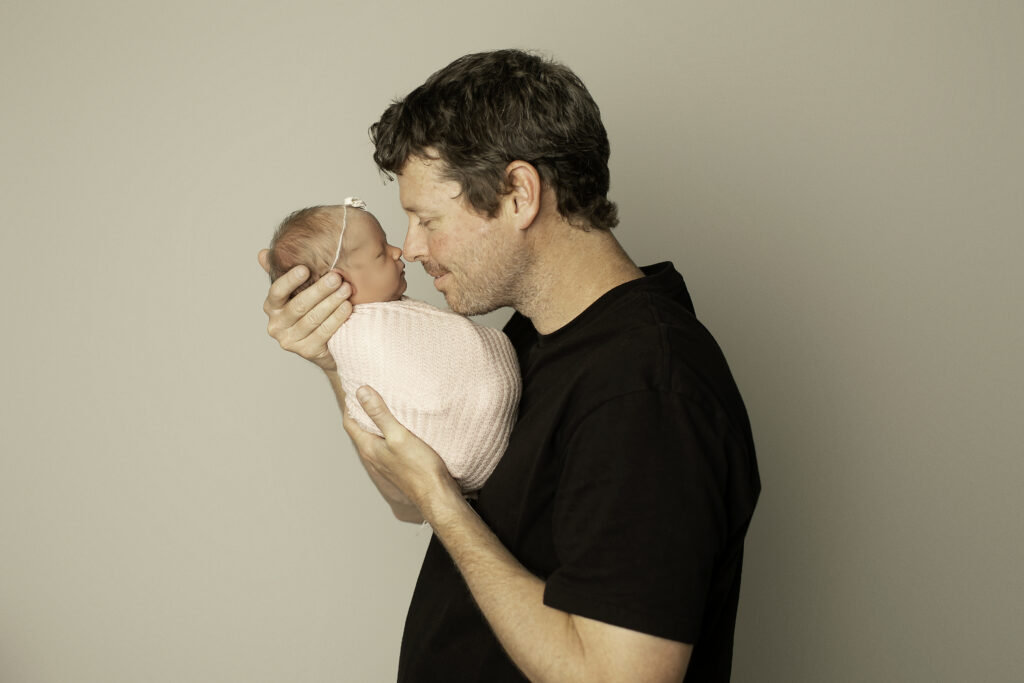 A proud dad cradles his newborn daughter, their bond shining through in this beautiful, tender moment captured by Chunky Monkey Photography