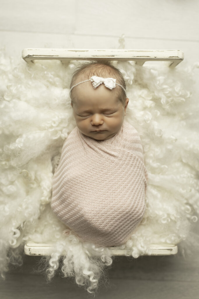 A sweet newborn girl resting gently in a soft, cozy bed, her delicate features captured beautifully by Chunky Monkey Photography.