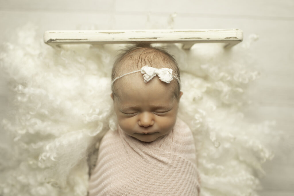 A newborn girl peacefully sleeping in a cozy bed, wrapped in soft blankets, captured in a tranquil moment by Chunky Monkey Photography