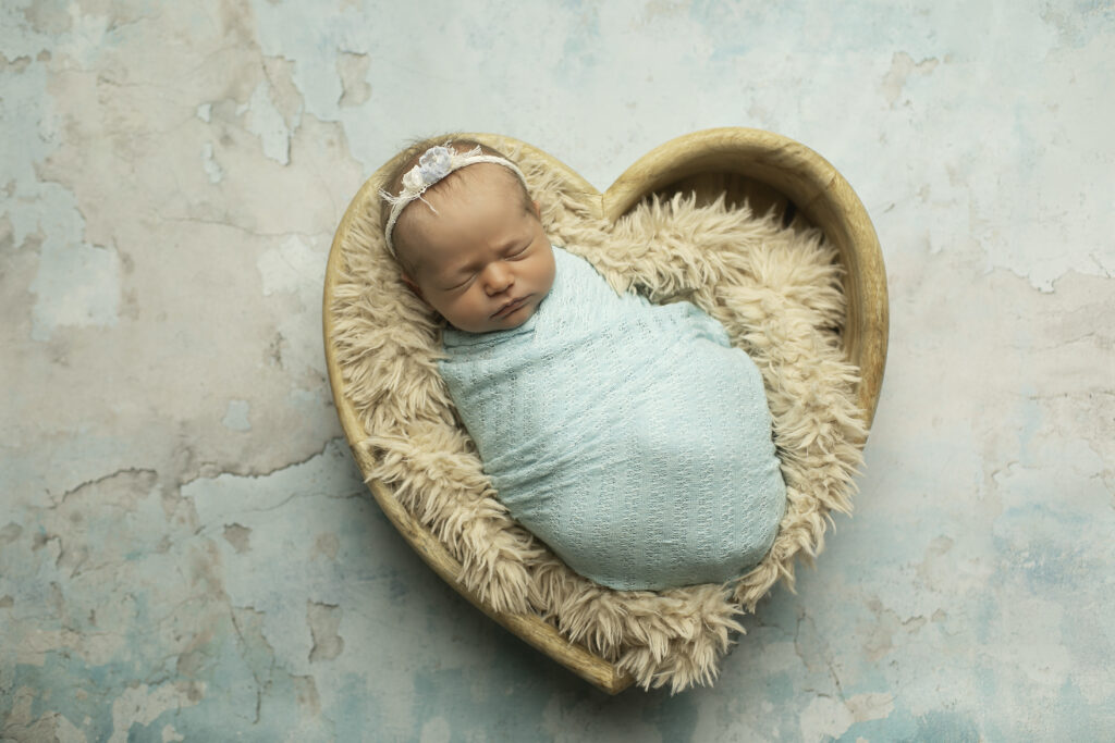 A newborn girl curled up in a heart-shaped prop, radiating sweetness and love, beautifully captured by Chunky Monkey Photography