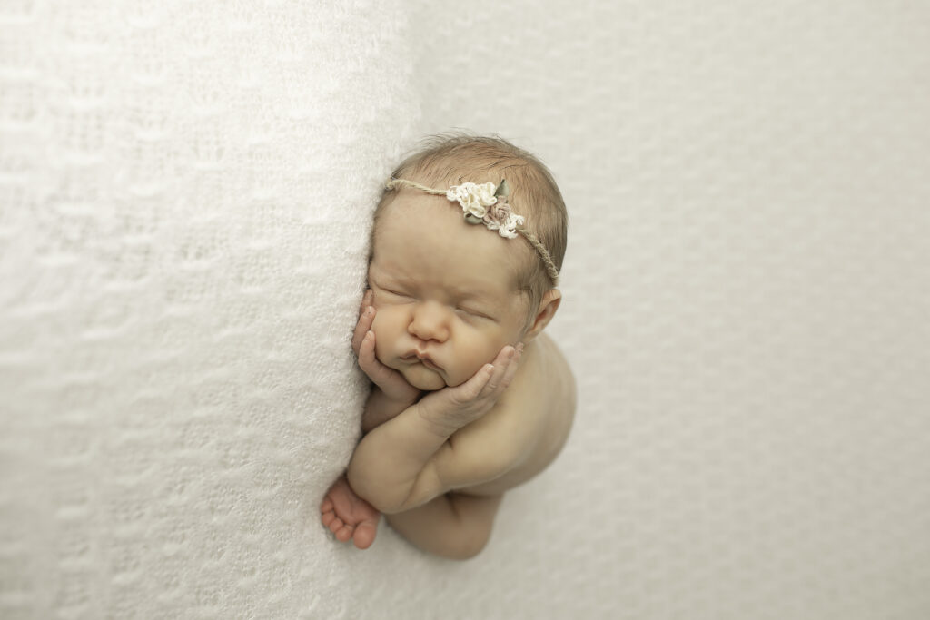 A newborn girl peacefully resting on a soft white blanket, captured in a simple, serene pose by Chunky Monkey Photography