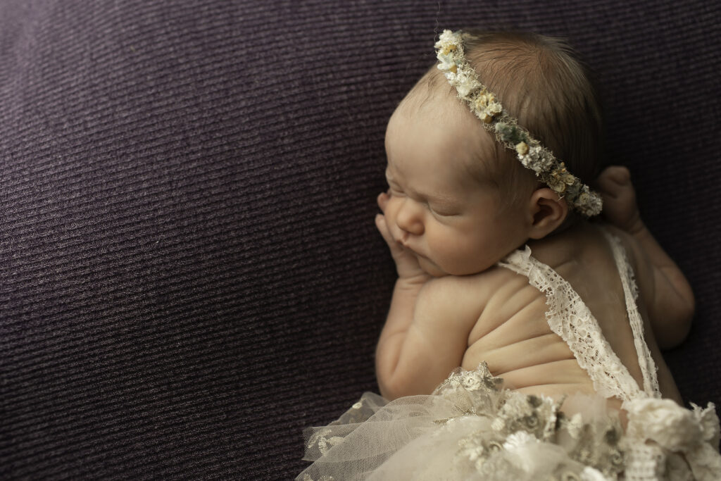 A serene moment with a newborn girl lying on her side, wrapped in a cozy blanket, captured by Chunky Monkey Photography