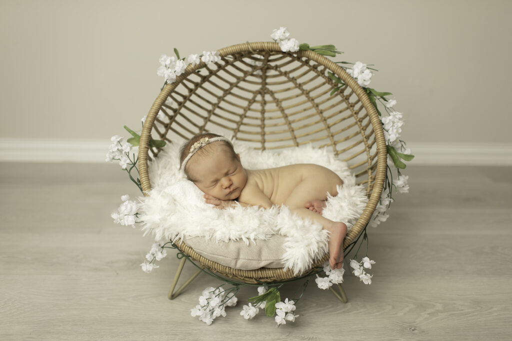 A newborn girl peacefully nestled in a wicker basket, wrapped in a soft blanket, captured in a serene moment by Chunky Monkey Photography