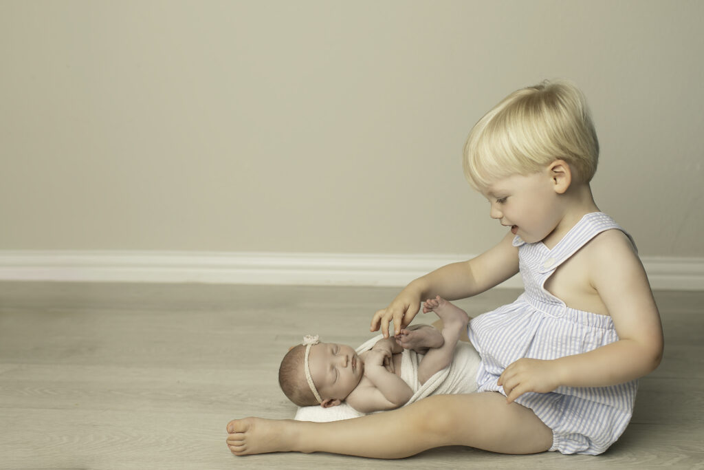 A big brother gently holds his newborn sister in his arms, showing his affection and excitement for her, captured beautifully by Chunky Monkey Photography