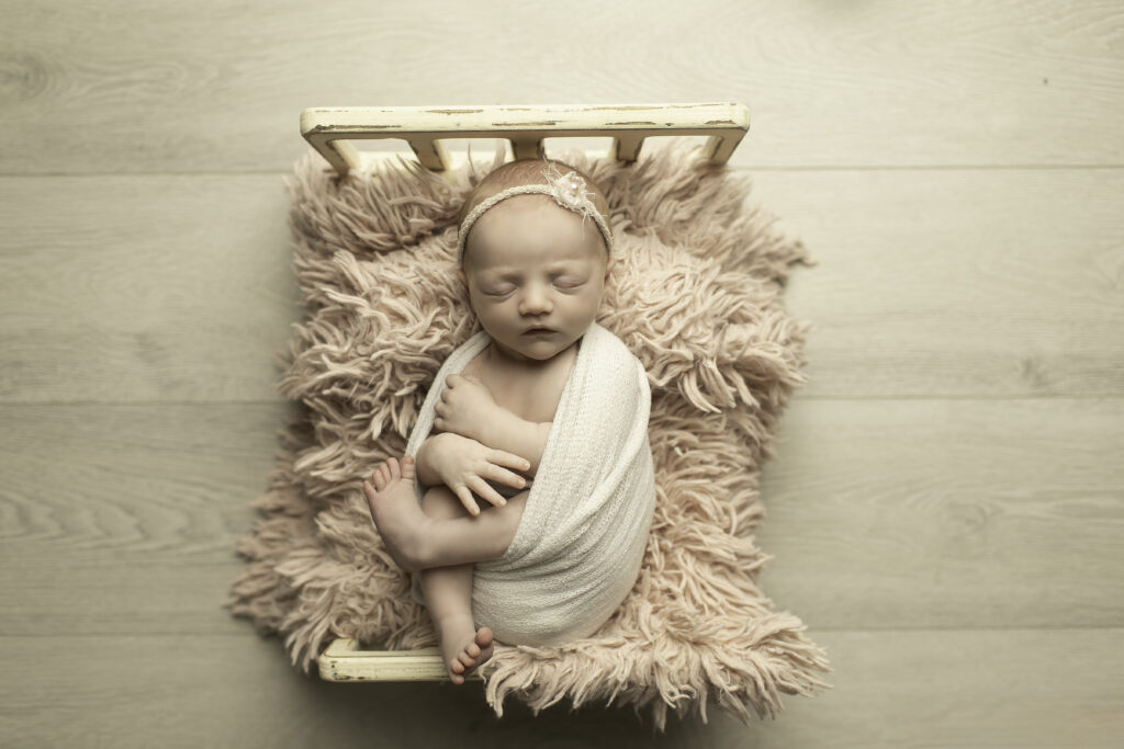 A sweet newborn girl lying gently in bed, surrounded by softness and warmth, her delicate features captured beautifully by Chunky Monkey Photography.