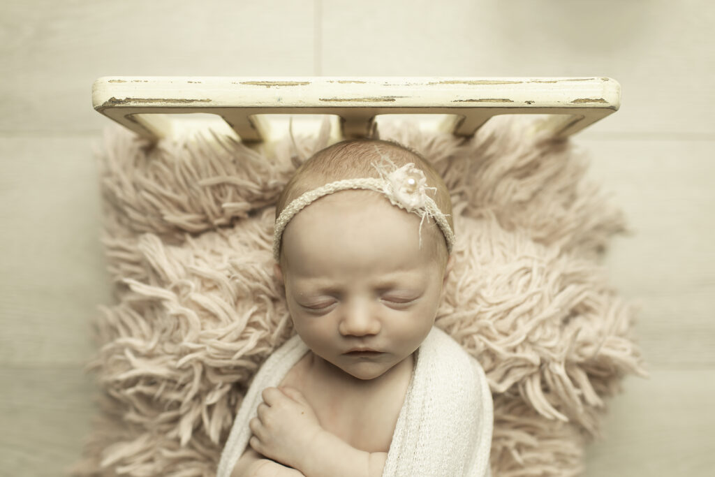 A newborn girl peacefully sleeping in a cozy bed, wrapped in soft blankets, captured in a serene moment by Chunky Monkey Photography.