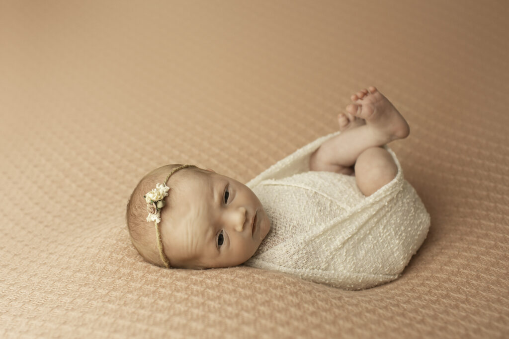 In a soft, cozy pink blanket, a newborn girl is captured in a peaceful, simple pose, showcasing her delicate beauty