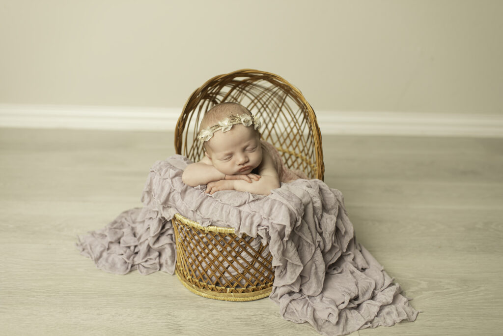 In a cozy wicker basket, a newborn girl is peacefully posed, capturing the serenity of the moment with Chunky Monkey Photography