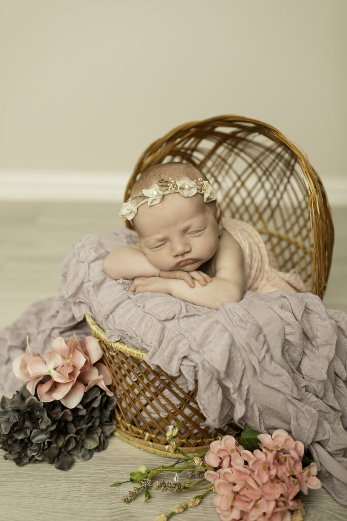 Chunky Monkey Photography captures a newborn girl resting in a wicker basket, her delicate features highlighted in this soft and timeless pose