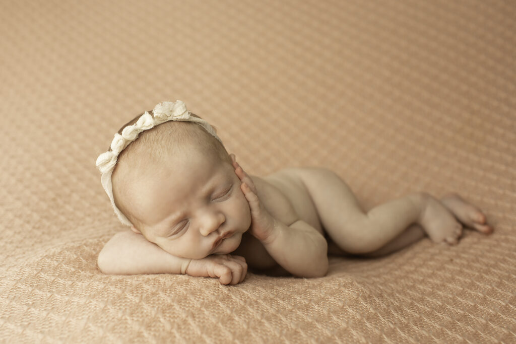 A newborn girl peacefully posed on a soft pink blanket, captured in a serene moment by Chunky Monkey Photography.