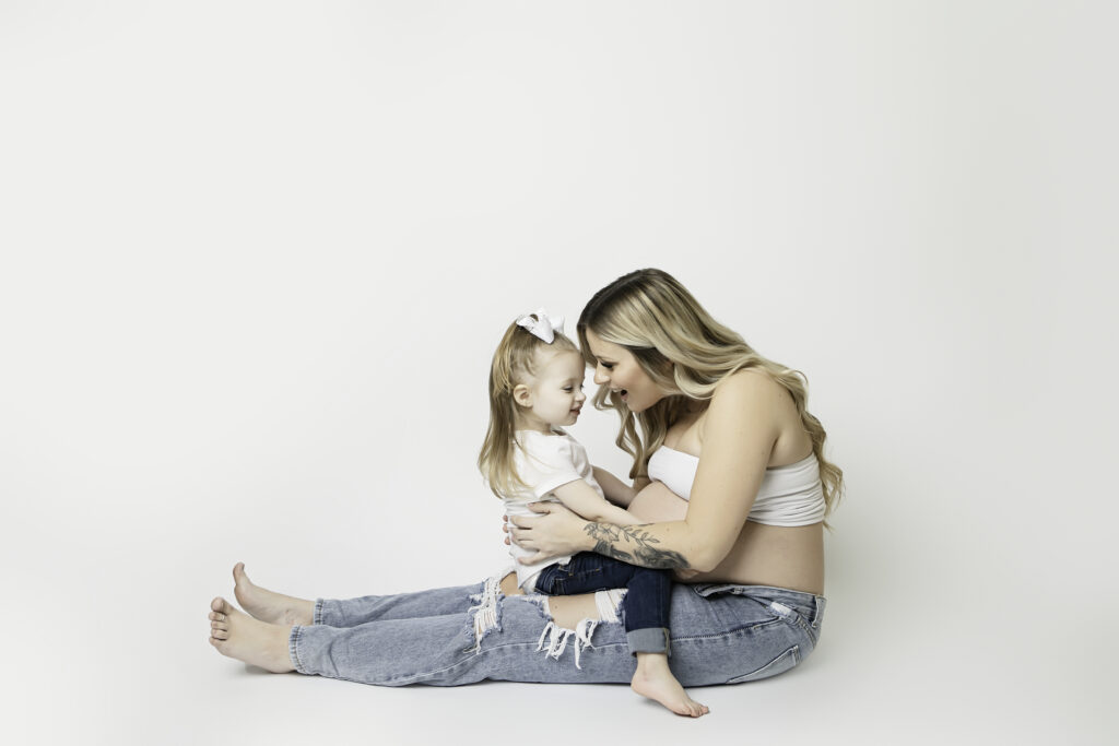 Big sister sharing a sweet moment with her pregnant mom in a studio maternity photoshoot, radiating excitement for the new baby