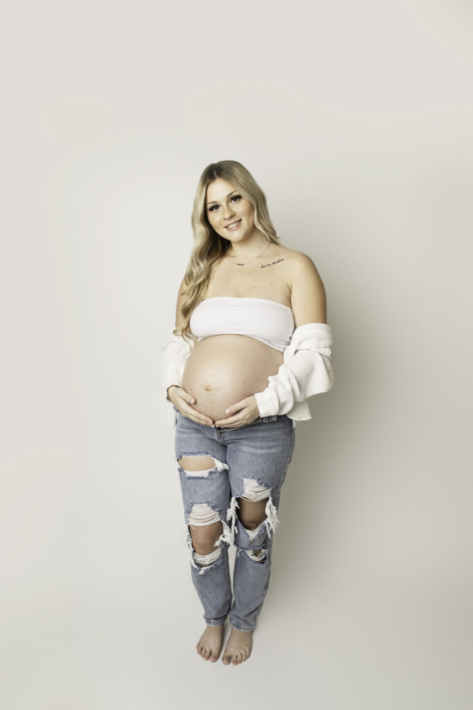 Expecting mother in a stunning studio maternity session, elegantly posed with soft lighting highlighting her baby bump