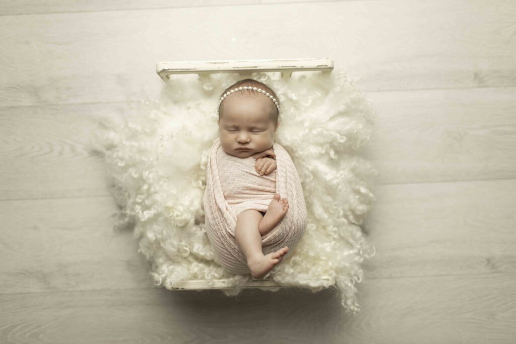 Newborn peacefully swaddled and lying on a cozy bed, surrounded by soft textures.