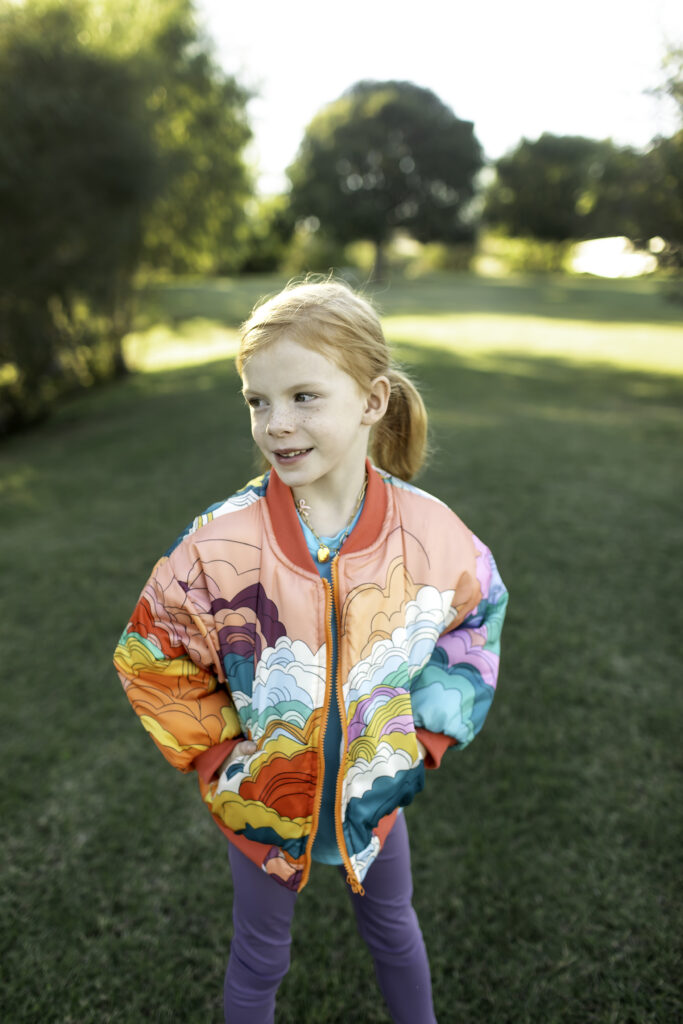 6-year-old girl in a colorful jacket, laughing while running through the park