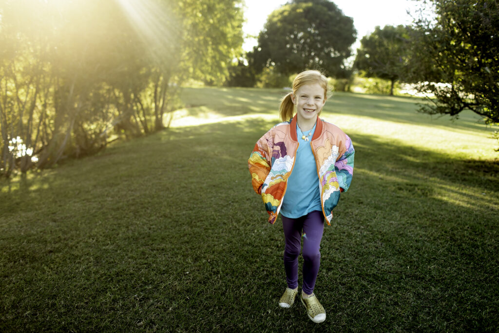 Happy 6-year-old girl in a colorful jacket, twirling around in the park surrounded by birthday decorations