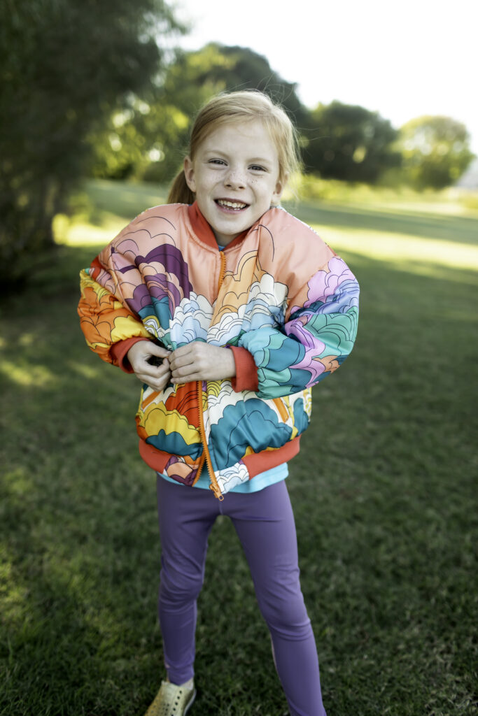 6-year-old girl in a colorful jacket, playing on the swings at the park with a big smile