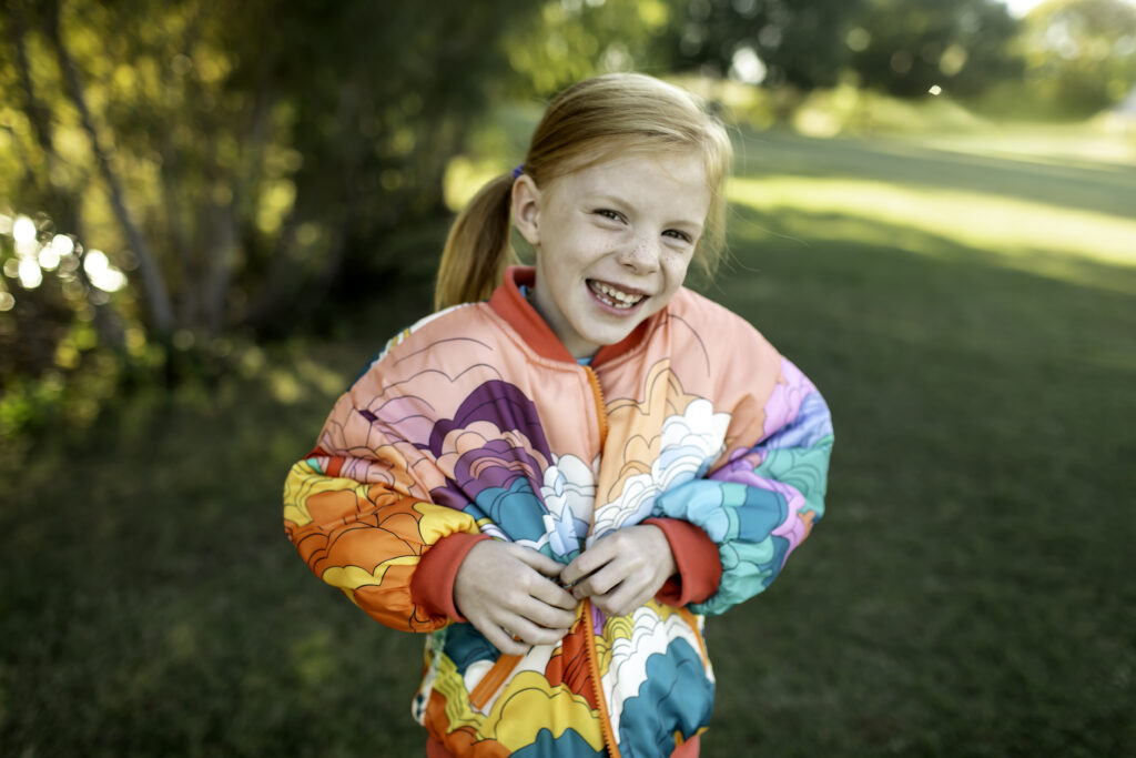 6-year-old girl wearing a colorful jacket, swinging at the park during her birthday celebration