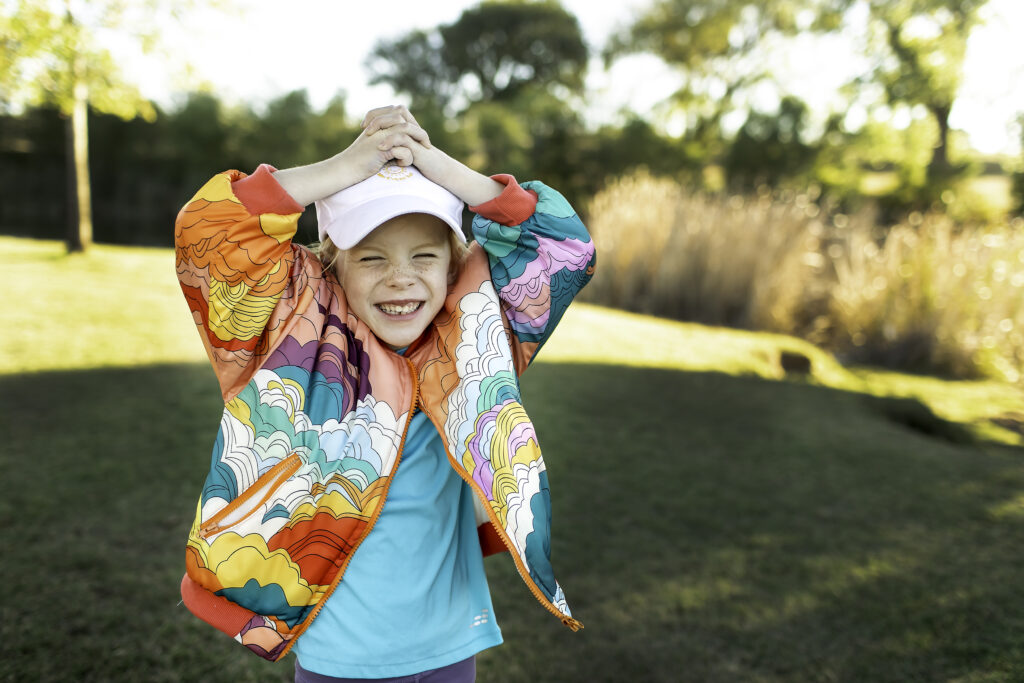 6-year-old girl in a colorful jacket, smiling joyfully while playing at the park on her birthday.