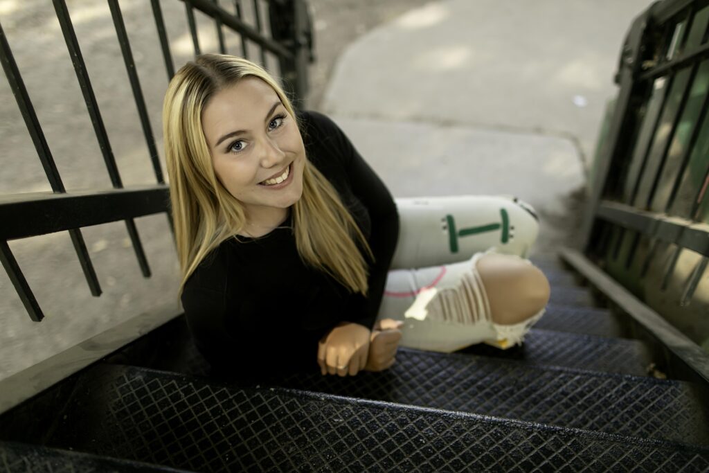 On sleek metal stairs in an urban setting, a senior girl smiles as the Fort Worth skyline contrasts with the modern, industrial backdrop of her photoshoot