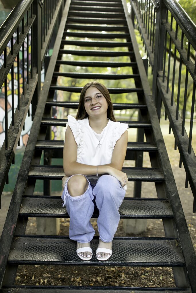 Senior girl confidently posing on metal stairs at Trinity Park, dressed in a white shirt and blue jeans