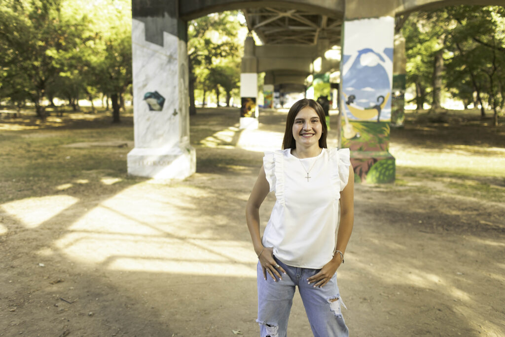 Senior girl smiling confidently in a white shirt and blue jeans at Trinity Park