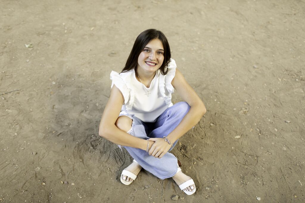 Relaxed portrait of senior girl with the park’s greenery in the background, wearing a white shirt and blue jeans